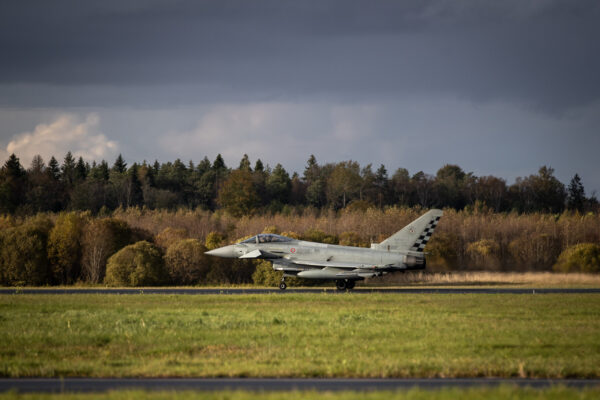 “Eurofighter Typhoon hävituslennuk takseerimas lennurajal sügisese metsa taustal.