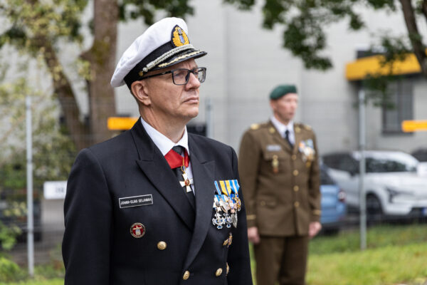 Pidulikus mereväe vormis ohvitser seisab tähelepanelikult välitseremoonial, rinnal teenetemärgid, taustal teine kaitseväelane rivis.
