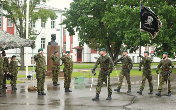 Kaitseväelased rohelises digilaigus vormis osalevad lipu ja mõõkadega pidulikul vahetustseremoonial kasarmuhoone ees vihmasel platsil.