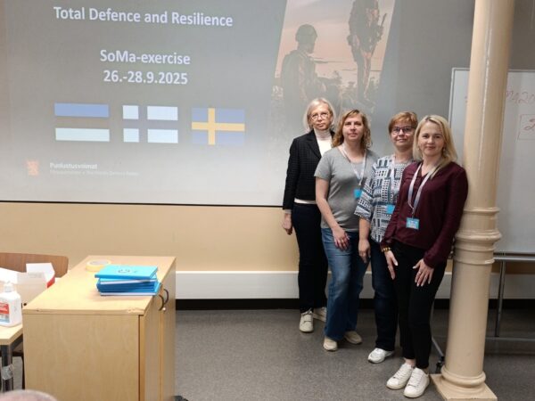 Neli naist seisavad paremal pool ettekande ekraani, mille pealkiri on "Total Defence and Resilience" Eesti, Soome ja Rootsi lipp .