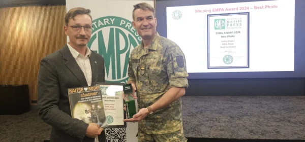 Kaks meest laval. paremalt sõjaväe vormis ja tema kõrval hallis pintsakus ja valges triiksärgis kaitse kodu esindaja. Mehed hoiavad oma käes auhinda, ajakirja ja diplomit