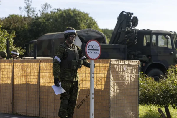 Kaitseväelane seisab stopp kontroll sildi kõrval, taustal on näha tara taga olevaid kaitseväe soomukeid